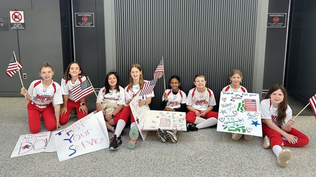 Inferno players holding American flags and thank-you signs at the airport welcoming Honor Flight veterans